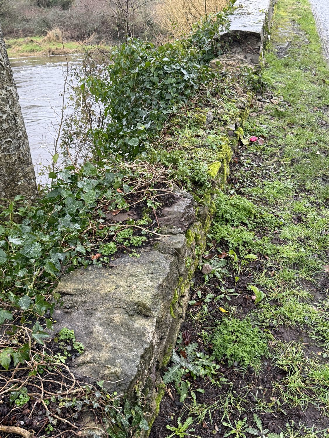 The parapet reduced to rubble, a displaced stone at its base and the capping gone — the river directly beyond.